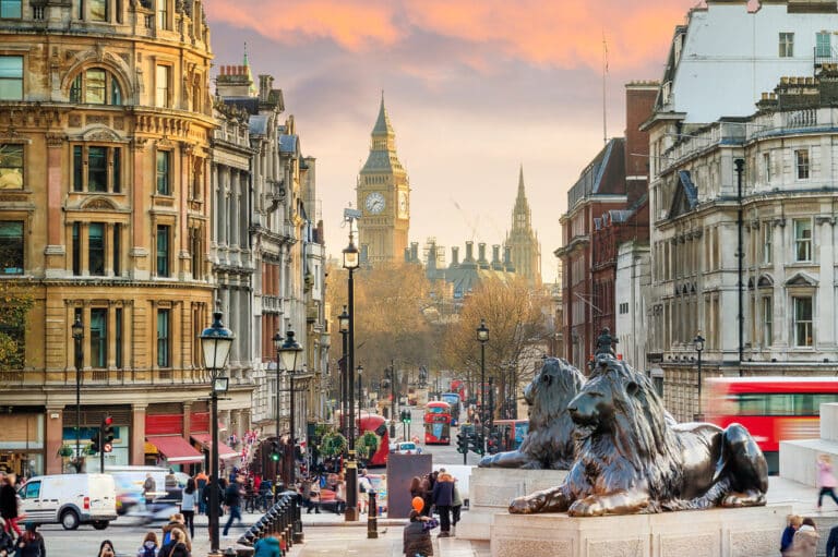 A bustling city street in London at sunset, featuring the iconic Big Ben and a nearby hair loss clinic. Double decker buses and cars mingle on the road, while bronze lion statues stand proudly in the foreground, framed by historic buildings and lush trees.